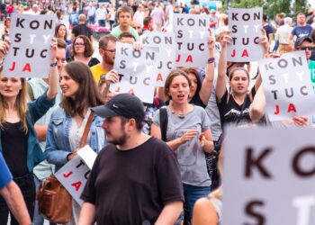 Ellerinde 'Konstytucja' yazılı pankartlar taşıyan kalabalık bir grup insan protesto yürüyüşü yapıyor.