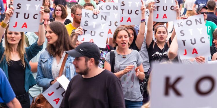 Ellerinde 'Konstytucja' yazılı pankartlar taşıyan kalabalık bir grup insan protesto yürüyüşü yapıyor.