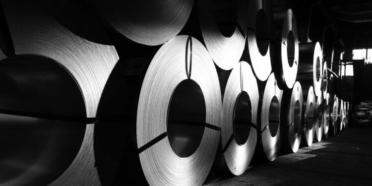 Fabrikada düzenli şekilde üst üste dizilmiş büyük metal rulo saçlar.