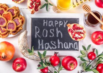 Üzerinde Happy Rosh Hashanah yazan kara tahta ve etrafında elmalar, nar ve bal.