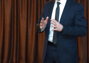 Koyu takım elbise giymiş bir adam ellerini anlatım yaparken gösteriyor.