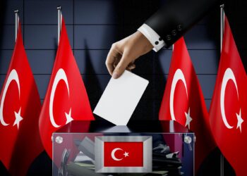 Takım elbiseli bir kişinin oy pusulasını şeffaf oy sandığına attığı an.