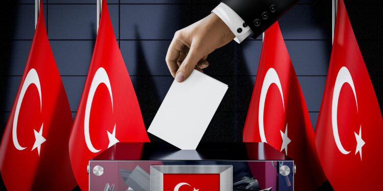Takım elbiseli bir kişinin oy pusulasını şeffaf oy sandığına attığı an.
