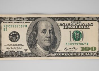 Gri zemin üzerinde duran tek bir yüz dolar banknotu