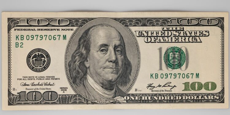 Gri zemin üzerinde duran tek bir yüz dolar banknotu