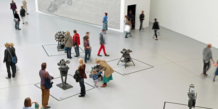 Geniş bir müzede sanat eserlerini ve sergileri gezen ziyaretçiler.