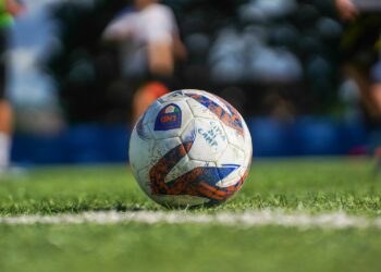 Çim sahada oyuncuların mücadelesi sırasında duran renkli futbol topu.