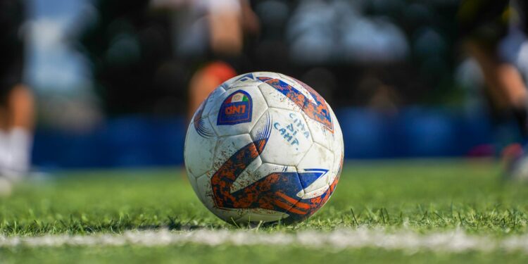 Çim sahada oyuncuların mücadelesi sırasında duran renkli futbol topu.