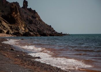 Dağların eteğinde dalgalı denizin ve kumsalın uzandığı geniş sahil manzarası.