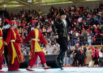 Halk oyunları kıyafetleri giymiş çocuk dansçılar açık havada neşeyle dans ediyor.