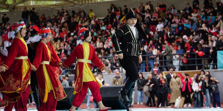 Halk oyunları kıyafetleri giymiş çocuk dansçılar açık havada neşeyle dans ediyor.