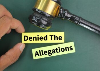 Bir elin tuttuğu sarı blok üzerinde 'Denied The Allegations' yazısı ve mahkeme tokmağı bulunuyor.