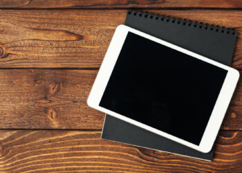 Ahşap masa üzerinde siyah ekranlı beyaz tablet ve siyah bloknot