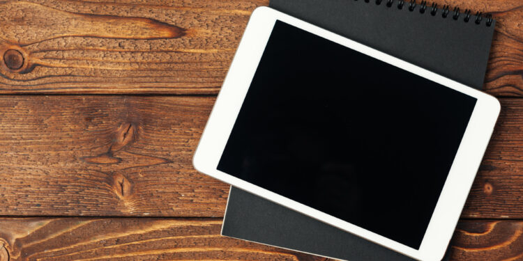 Ahşap masa üzerinde siyah ekranlı beyaz tablet ve siyah bloknot