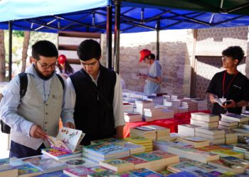 Açık havadaki bir kitap fuarı tezgahında kitap inceleyen insanlar.