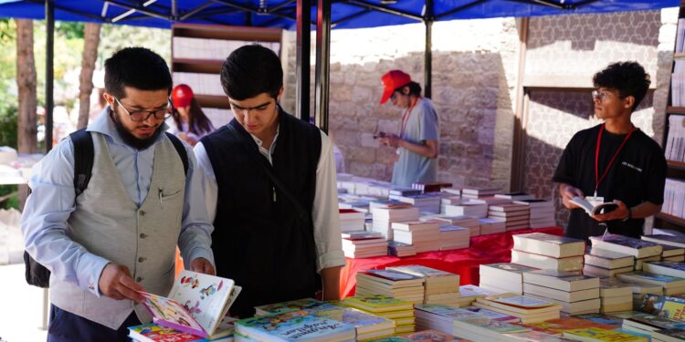 Açık havadaki bir kitap fuarı tezgahında kitap inceleyen insanlar.