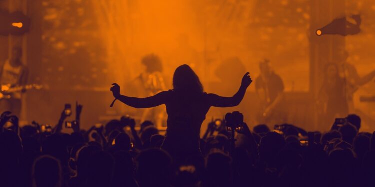 Konser alanında ellerini kaldıran kalabalık ve sahne ışıkları altında kalabalık.