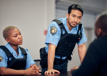 Polis memurları bir kişiyle konuşurken masanın başında duruyor.