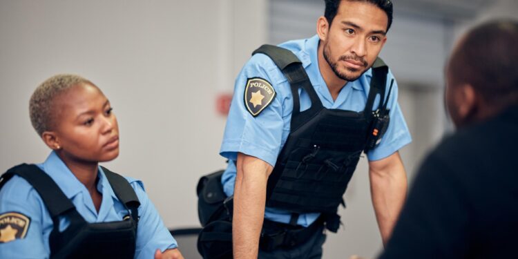 Polis memurları bir kişiyle konuşurken masanın başında duruyor.