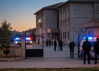 Akşam karanlığında okul bahçesinde güvenlik önlemi alan polis ekipleri ve kalabalık.