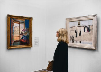 Müzede sergilenen tabloları inceleyen sarışın bir kadın ziyaretçi.