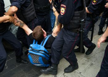 Rus polis üniformalı görevliler sokakta bir kişiyi yere yatırıp gözaltına alıyor.