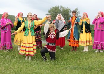 Halk oyunları kıyafetleri giymiş bir grup insan müzik eşliğinde folklor oynuyor.