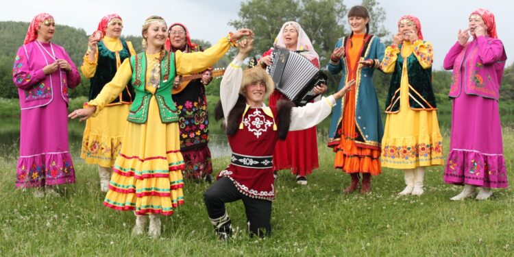 Halk oyunları kıyafetleri giymiş bir grup insan müzik eşliğinde folklor oynuyor.