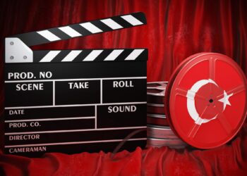 Kırmızı fon önünde duran siyah bir sinema klaketi ve makara.