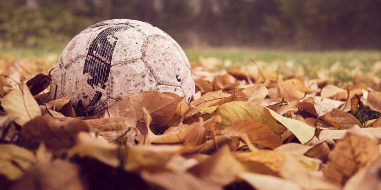Sonbahar yaprakları arasında yerde duran eski ve çamurlu futbol topu