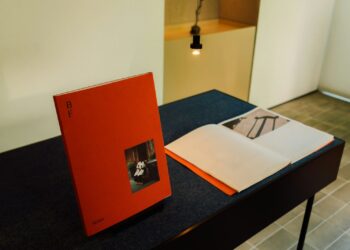 Kırmızı bir sanat kitabı ve açık durumda sergilenen katalog masada duruyor.