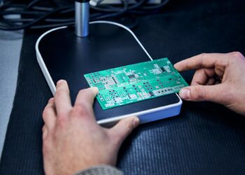 Masada iki elle tutulan yeşil renkli elektronik devre kartı yakın çekimi.